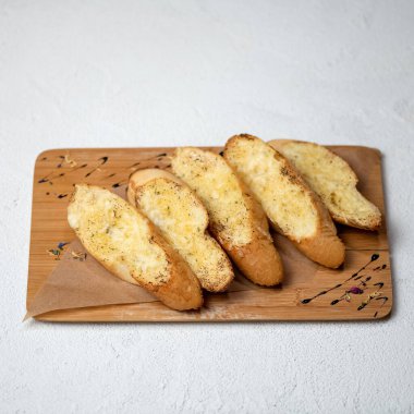 Tahta kesme tahtasının üzerinde sarımsak soslu ekmek kırıntıları. Beyaz arkaplanda kızarmış ekmek