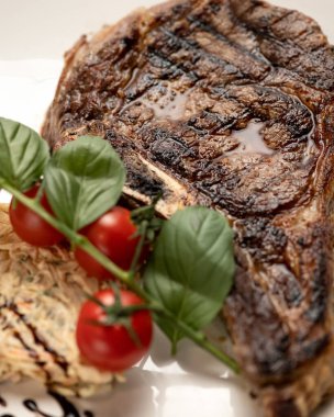 Izgara et bifteği. Domatesli pirzola ya da sığır filetosu ve beyaz tabakta fesleğen. Dikey format. Yumuşak odak