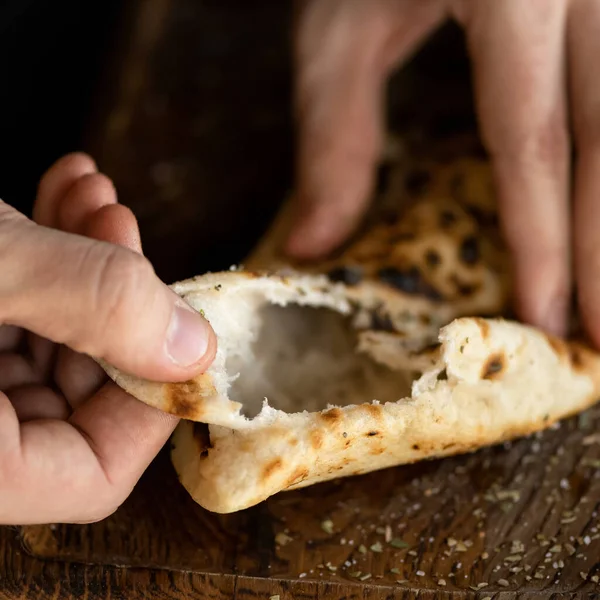 Male hands breaking baked crispy hot pita bread on wooden table. Close-up shot. Soft focus — Stock Photo, Image