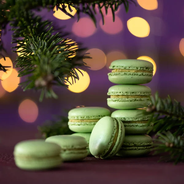 Macaroons de sobremesa franceses. Conceito de Natal e Ano Novo. Doces verdes e raminho de abeto no fundo lilás borrado com bokeh. Blank ou modelo para cartão de saudação. Espaço para cópia. Foco suave — Fotografia de Stock