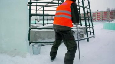 Turuncu yelekli bir işçi arabasından buz parçaları indirmekle meşgul..