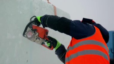 Ellerinde elektrikli testereyle koruyucu bir miğfer takmış işçi derleyicisi buz kalıbını keser.