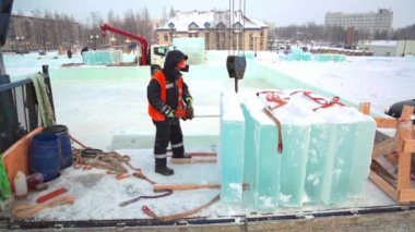 Koruyucu miğfer ve yansıtıcı yelek giyen bir işçi buz bloğunda benzopil ile bir delik açıyor.
