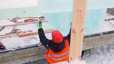 Ceketli ve kasklı bir askıcı buz kalıplarını boşaltıyor.