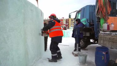 Ellerinde elektrikli testereyle koruyucu bir miğfer takmış işçi derleyicisi buz kalıbını keser.