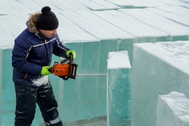 Elinde elektrikli testereyle çalışan bir işçi, buz bloğunun altını oyuyor.