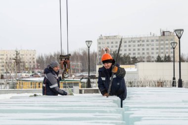 Turuncu kasklı bir işçi, buz kalıplarını levyeyle itiyor.