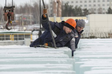 Turuncu kasklı bir işçi, buz kalıplarını levyeyle itiyor.