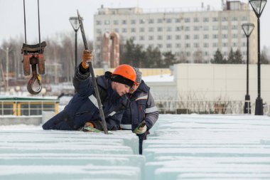Turuncu kasklı bir işçi, buz kalıplarını levyeyle itiyor.