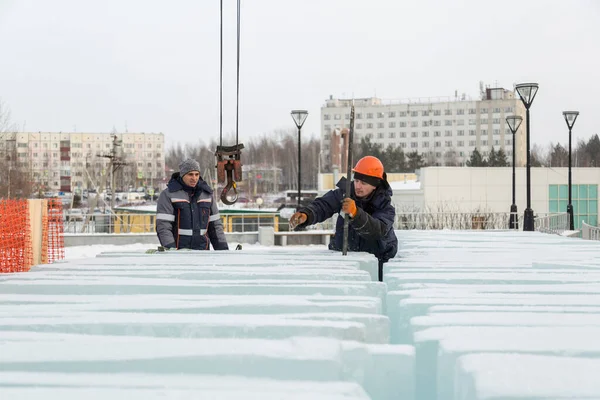 A worker in an orange helmet pushes the ice blocks apart with a crowbar