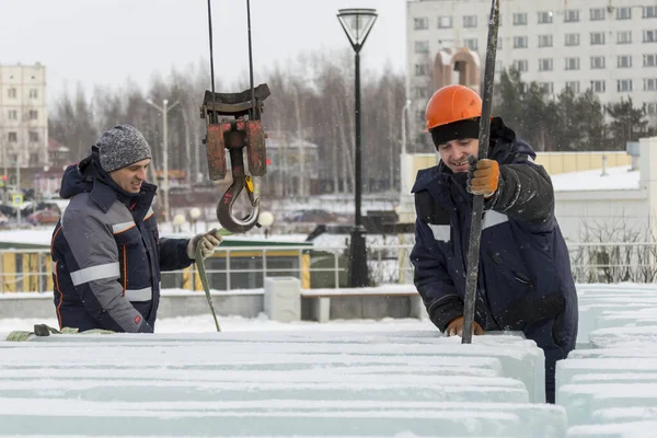 A worker in an orange helmet pushes the ice blocks apart with a crowbar