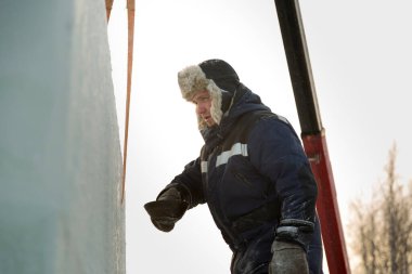 Mavi kışlık ceketli, açık renk kürklü bir şapkayla bir buz kasabasının buz panellerini birleştiriyor.