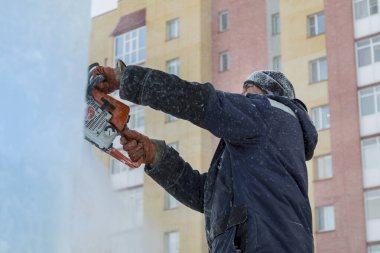 Mavi ceketli bir montaj işçisi ve siyah örülmüş bir şapka bir buz tabakasını testere ile düzeltiyor.