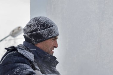 Mavi ceketli ve buz panelinin yanında örülmüş siyah şapkalı bir montajcının portresi.