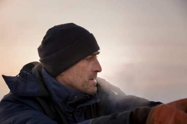 Kafasında siyah örgü şapkalı mavi ceketli bir tesisatçının portresi.