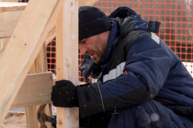 Kulaklıklı bir şapka takan biri ahşap kirişlerden yapılmış bir kaydırağın çerçevesini monte eder.
