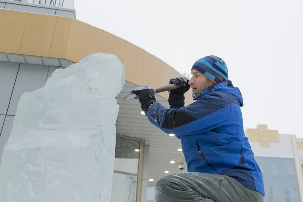 The sculptor cuts an ice figure out of a block of ice for Christmas