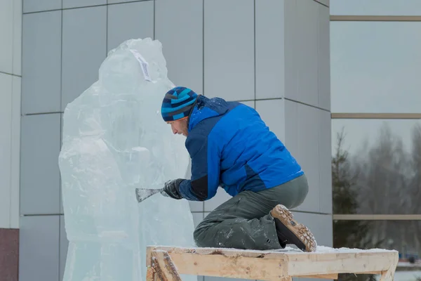 The sculptor cuts an ice figure out of a block of ice for Christmas