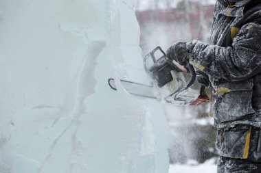 Heykeltıraş, buzdan bir buz figürünü Noel için elektrikli testere ile kesiyor.
