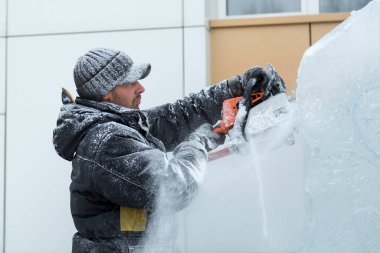 Heykeltıraş, buzdan bir buz figürünü Noel için elektrikli testere ile kesiyor.