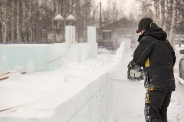 Heykeltıraş, buz bloğundan benzin testeresiyle bir figür kesiyor.