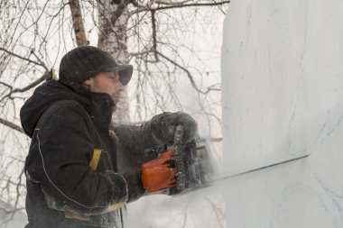 Heykeltıraş, buz bloğundan benzin testeresiyle bir figür kesiyor.