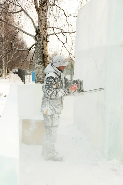Heykeltıraş, buz bloğundan benzin testeresiyle bir figür kesiyor.
