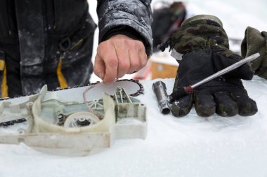 Kışın çalışan bir işçi dışarıdaki elektrikli testereyi tamir eder.