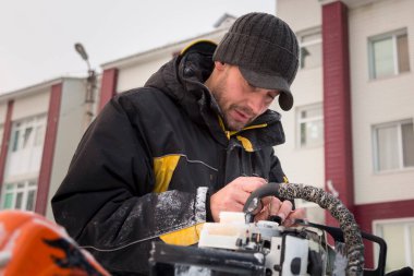Kışın çalışan bir işçi dışarıdaki elektrikli testereyi tamir eder.