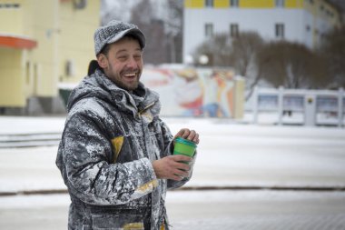 Elinde bir bardak sıcak kahveyle siyah şapkalı bir işçinin portresi.