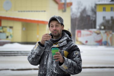 Elinde bir bardak sıcak kahveyle siyah şapkalı bir işçinin portresi.