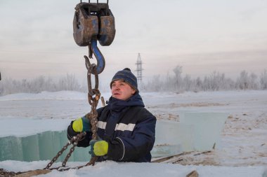 Mavi ceketli bir işçi fırlatıcısının portresi zincir örümceği kullanarak buz kalıplarını boşaltıyor.