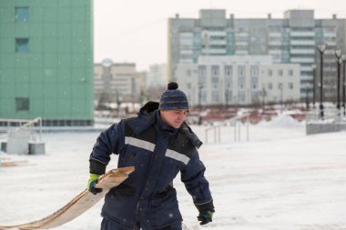 Elinde tahta olan mavi kapüşonlu bir müteahhit inşaat alanında yürüyor.