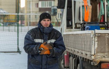 Arabanın yanında mavi ceketli ve siyah örgü şapkalı bir montajcının portresi.