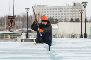 Turuncu kasklı bir işçi, buz kalıplarını levyeyle itiyor.