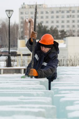 Turuncu kasklı bir işçi, buz kalıplarını levyeyle itiyor.