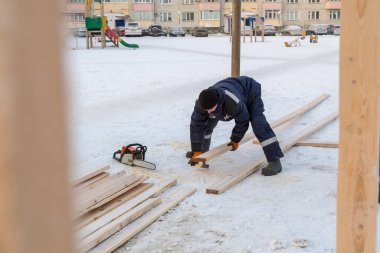 Mavi ceketli bir montajcı ahşap kirişlerden yapılmış bir kaydırağın çerçevesini monte eder.