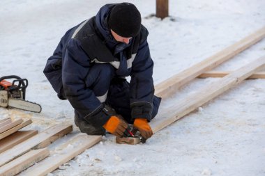 Mavi ceketli bir montajcı ahşap kirişlerden yapılmış bir kaydırağın çerçevesini monte eder.
