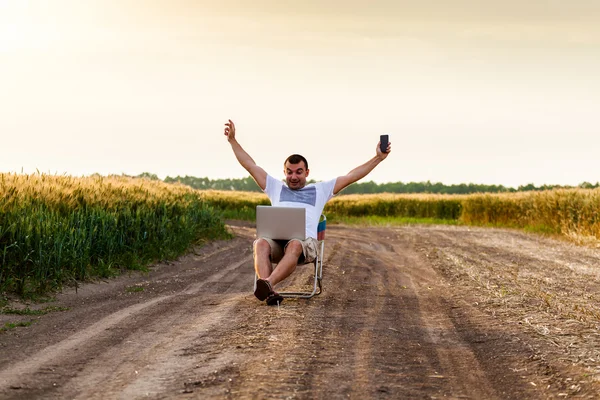 Businessman sitting in the field and working on laptop.