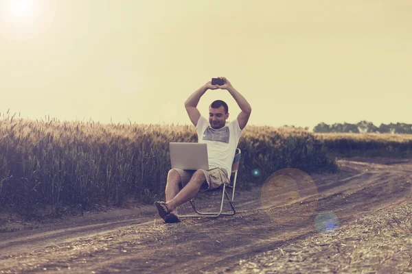 Businessman sitting in the field and working on laptop.