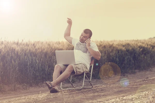 Businessman sitting in the field and working on laptop.