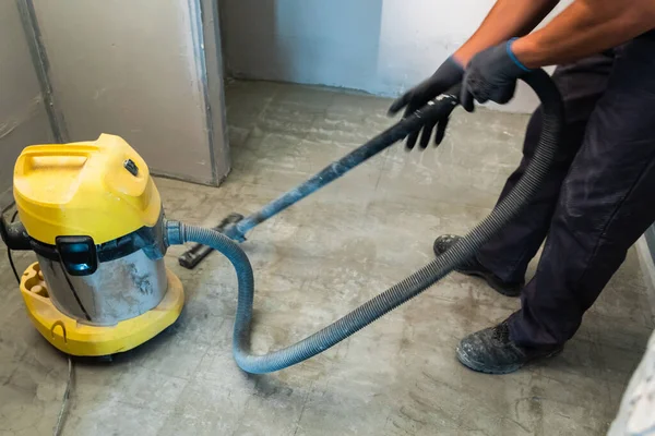The builder cleans the floor from dust with a construction vacuum cleaner. — Stock Photo, Image