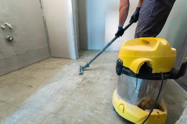 El constructor limpia el suelo del polvo con una aspiradora de construcción. — Foto de Stock