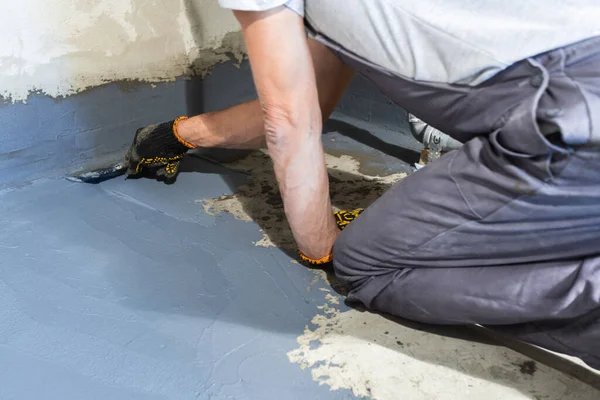 Um trabalhador construtor aplica uma argamassa de impermeabilização para o chão em uma sala. — Fotografia de Stock