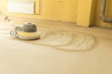 Depoda zımpara makinesiyle beton döşeme öğüten bir adam var.