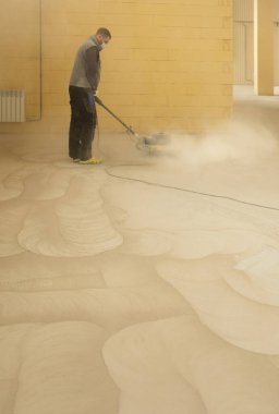 Depoda zımpara makinesiyle beton döşeme öğüten bir adam var.