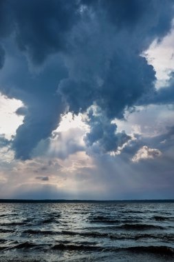 Fırtına bulutları ve güneş ışınları altında göl