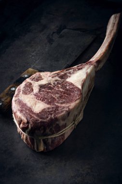 Çiğ Tomahawk bifteği. Eskimiş ve eskimiş. Arka planda bir et satırı var.