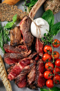 Tomahawk ızgara bifteği, tahtadan bir tahtada sebzelerle dilimlenmiş et barbeküsü pişiriyor.