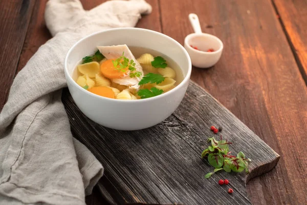 Makarnalı tavuk çorbası, havuç, maydanoz ve ahşap zemin üzerinde et parçaları. Ev yapımı köy çorbası.